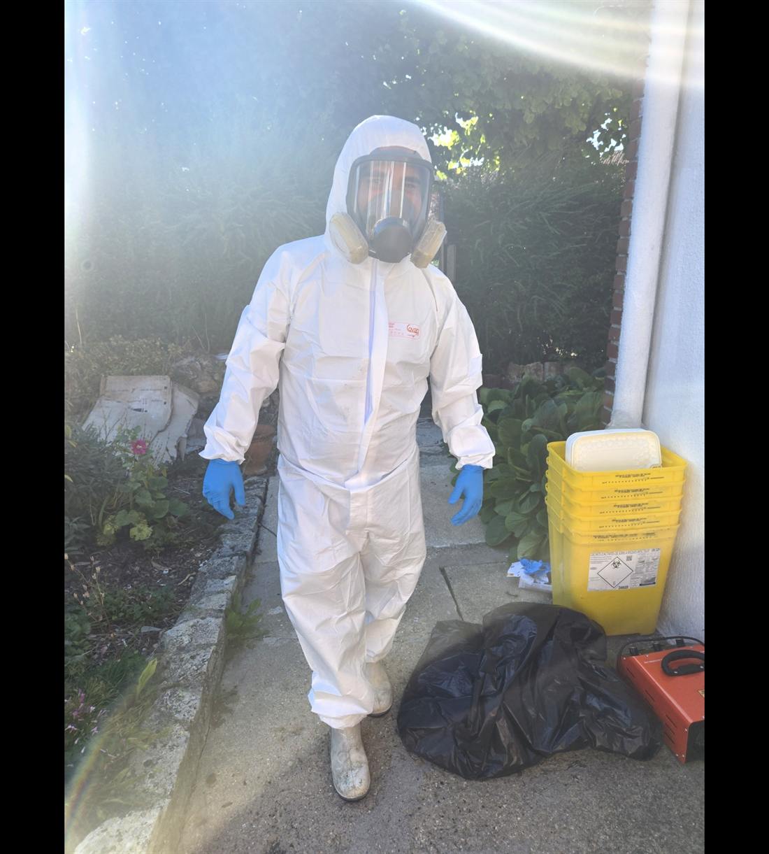 Technicien Serenza en combinaison intégrale et masque, avec conteneurs à déchets DASRI, prêt pour une décontamination