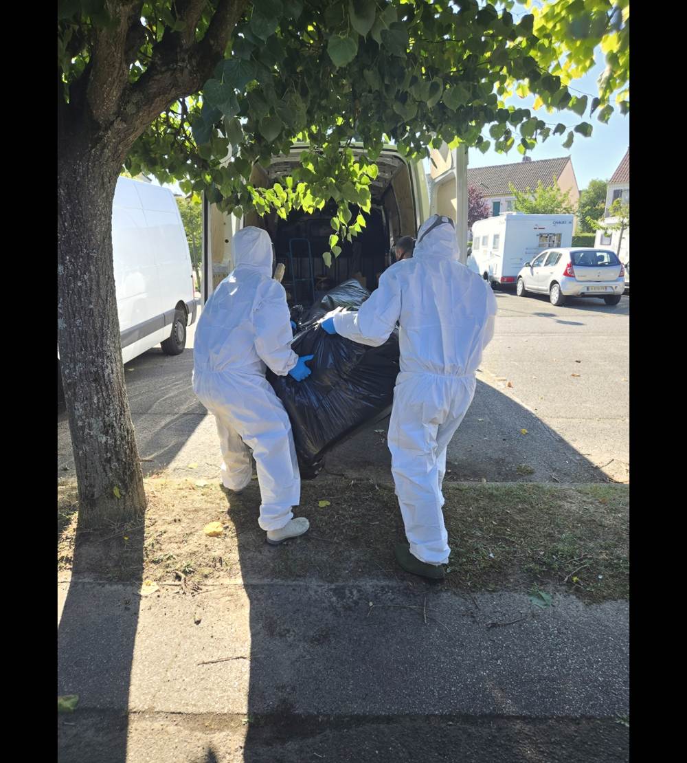Deux techniciens en combinaison, masque et gants évacuant les déchets d'une intervention de nettoyage après décès